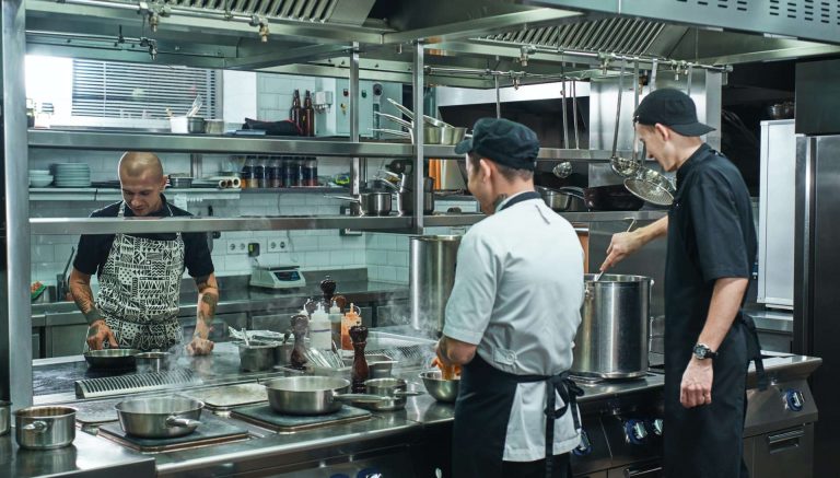 Cooking process. Professional team of chef and two young assistant preparing food in a restaurant